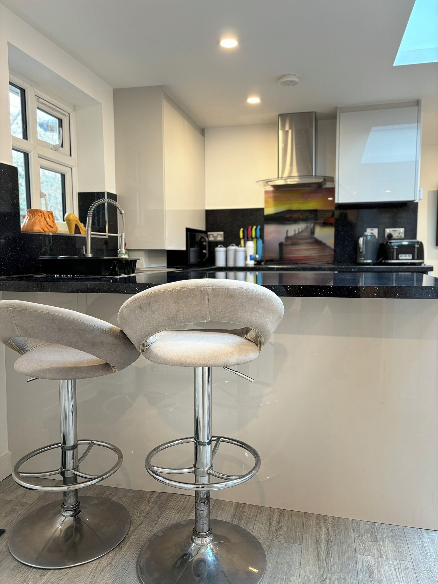 A modern kitchen with two bar stools, a stainless steel sink, and a range hood.