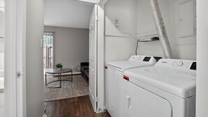 A laundry room with a washer and dryer, a small table with a plant, and a view to a balcony. - Comfortable  2BR space near shops and dining (Riverdale)