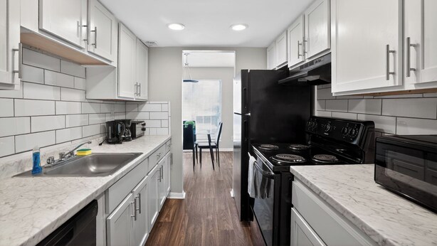 A modern kitchen with white cabinets, a black refrigerator, a stove, and a dishwasher. - Comfortable  2BR space near shops and dining (Riverdale)