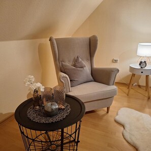 A modern living room with a high ceiling, a grey armchair, a small round table with decorative items, a white lamp on a side table, and a shaggy rug. - Cozy Holiday Apartment for 4 Guests with Free WiFi (Walkenried)