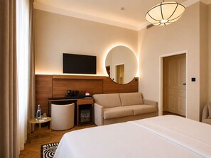 A hotel room with a bed, a sofa, a desk with a flat-screen TV, a mirror, and a round mirror. - Carlton Boutique Hotel Vienna - NEW OPENING (Vienna)