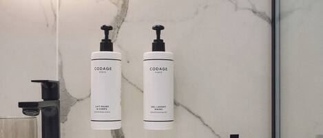 A bathroom with a white marble sink, two bottles of Codage hand cleansing gel, and a black faucet.
