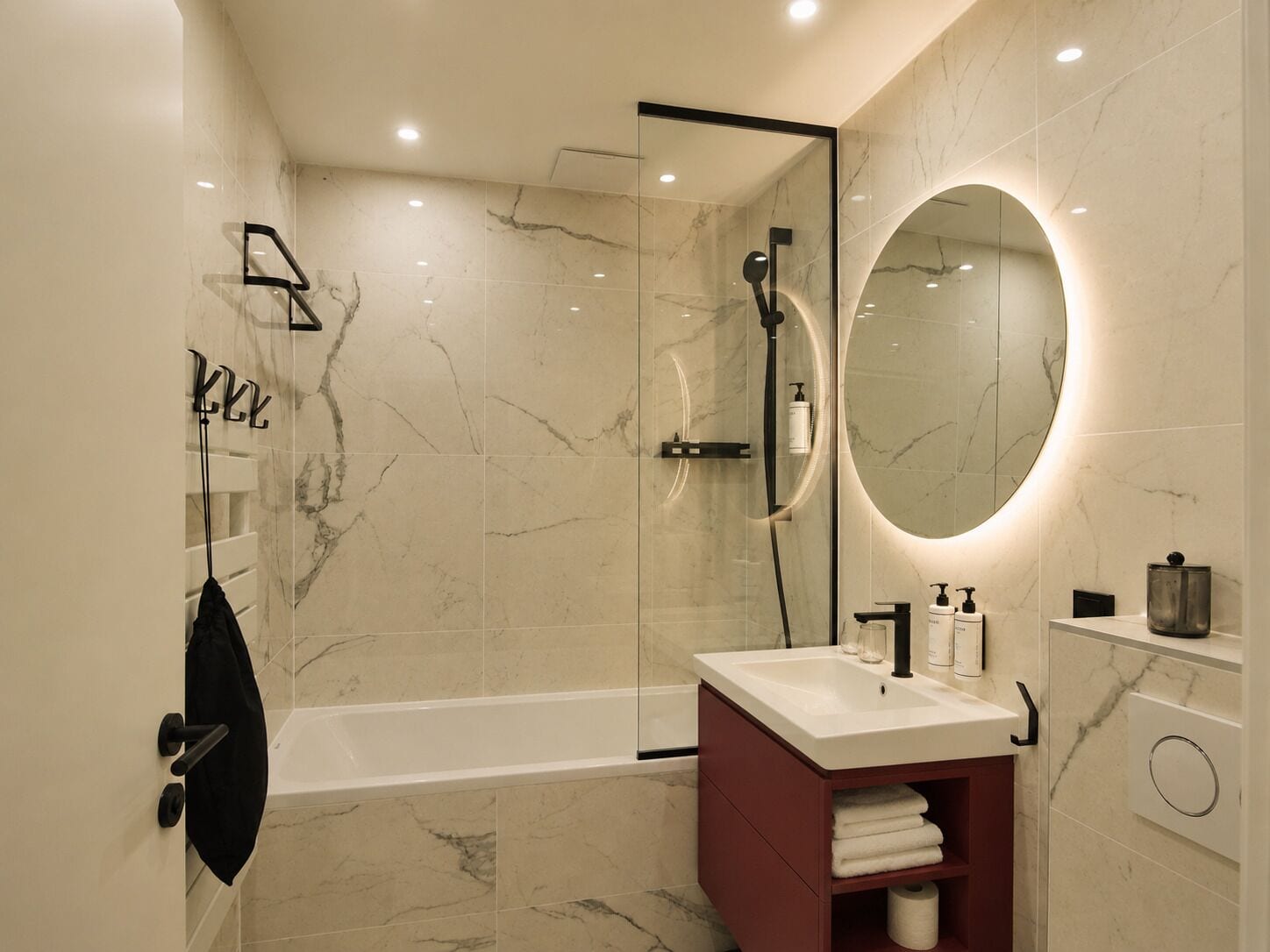 Un baño moderno con ducha envuelta en vidrio, un espejo redondo y un tocador con lavabo.