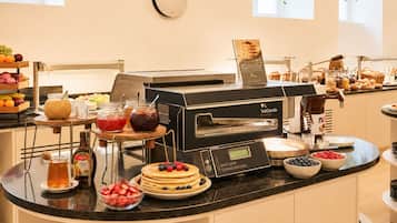 Un buffet de petit-déjeuner comprenant un appareil à gaufres, une machine à café et divers aliments.