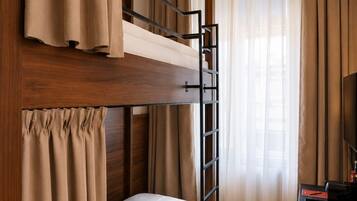 A bunk bed with a ladder, a desk with a computer, and a television in a room with wooden flooring and curtains.