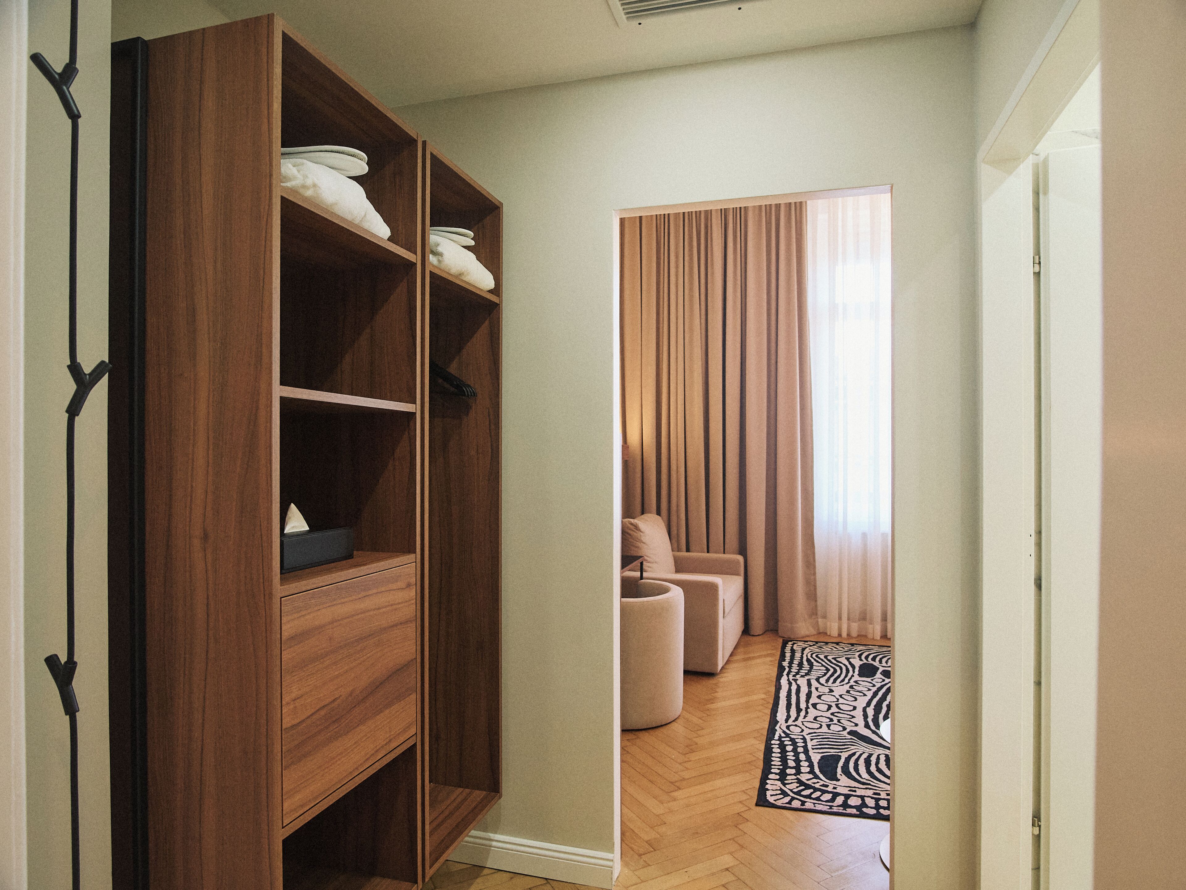 Una habitación con un armario de madera, una zona de estar con sofá y sillones, y una alfombra estampada en el suelo.