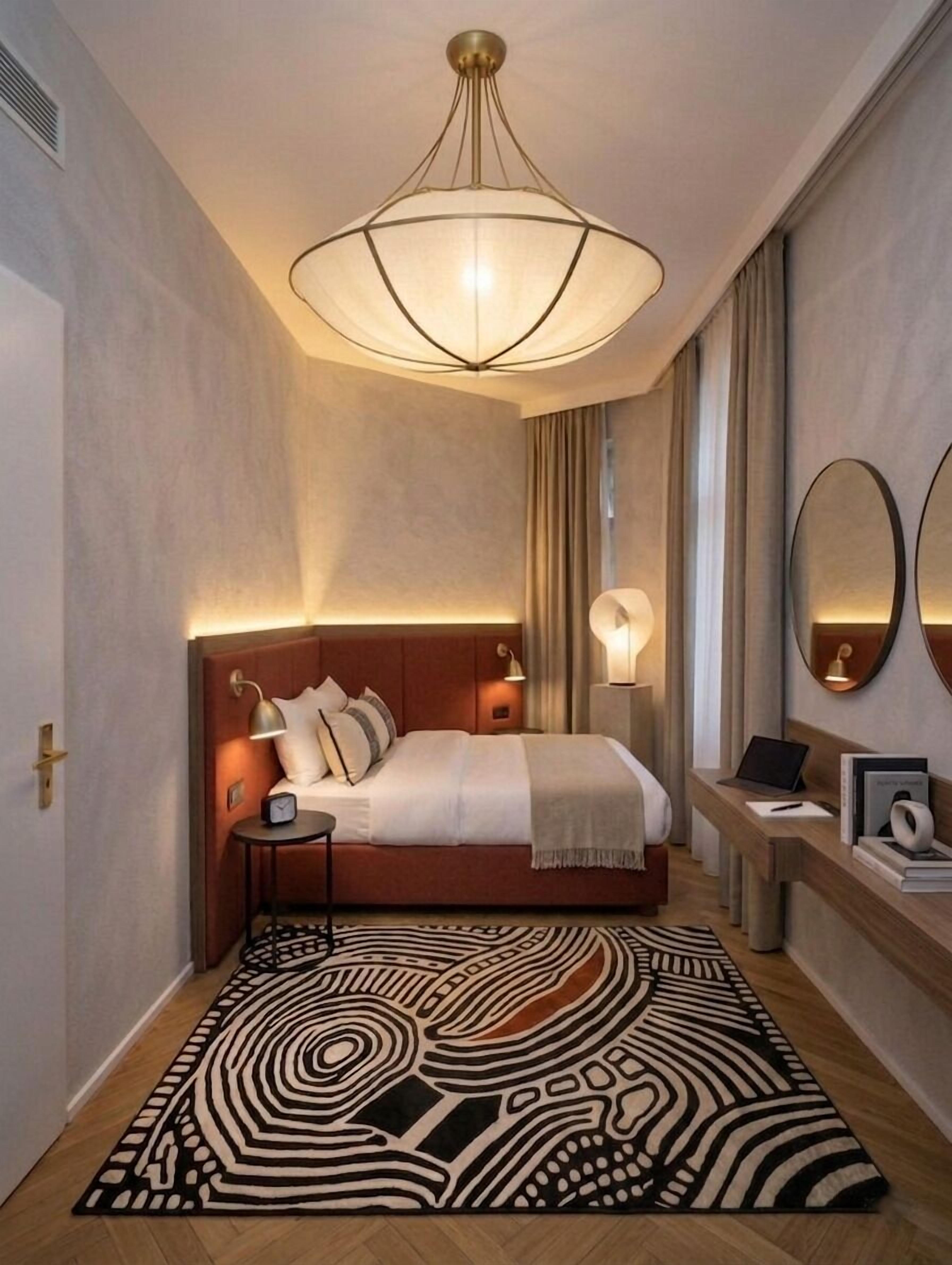 Un dormitorio moderno con una cama grande, lámparas de noche, una computadora portátil y una alfombra estampada.
