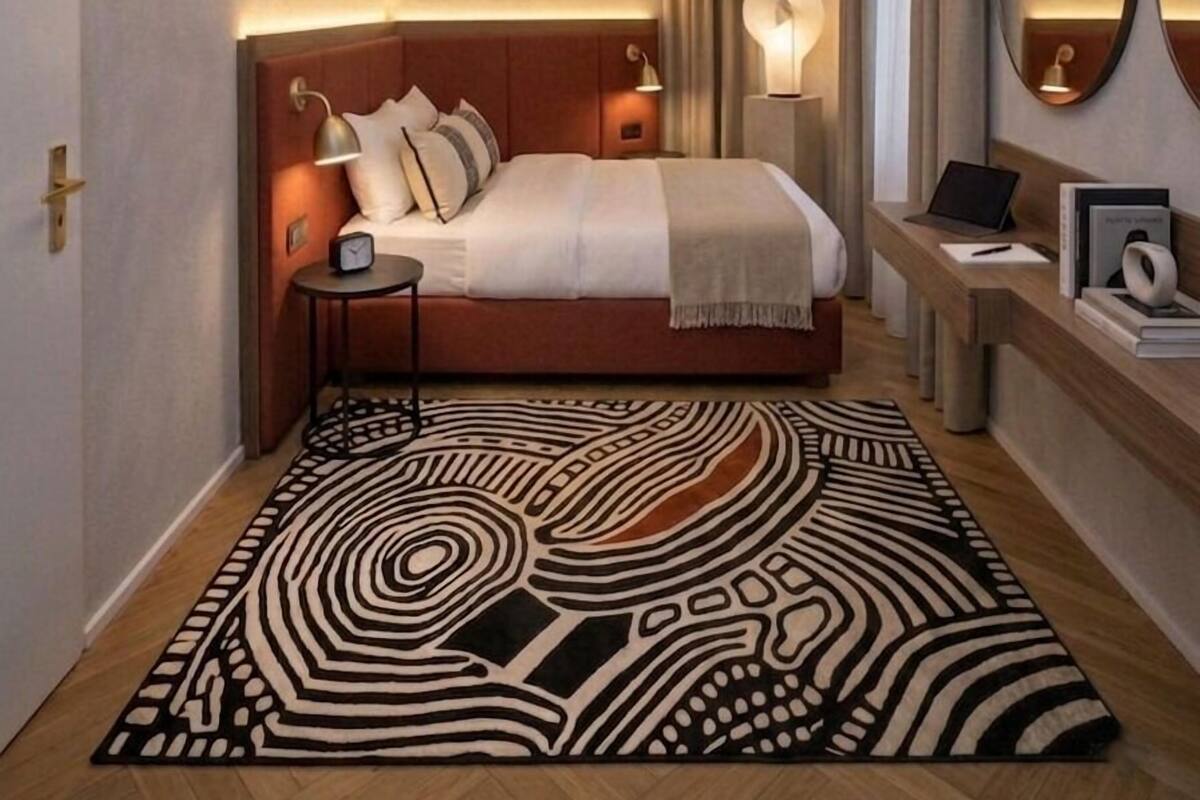 Un dormitorio moderno con una cama grande, lámparas de noche, una computadora portátil y una alfombra estampada.