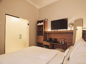 A hotel room with a bed, a desk, a mirror, and a wardrobe.