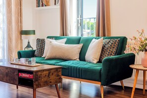 Ein grünes Sofa mit gemusterten Kissen, ein Holztisch und ein Beistelltisch mit einer Vase.