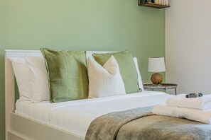 Ein Bett mit weißen und grünen Kissen, einer weißen Decke und einer grauen Tagesdecke.