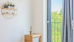 Ett rum med en hyllsektion i trä, en rund hylla som sitter på väggen och som har växter på sig, och en utsikt genom en balkongdörr.