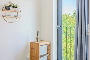Ein Zimmer mit einer Holzregaleinheit, einem runden Wandregal mit Pflanzen und Blick durch eine Balkontür.