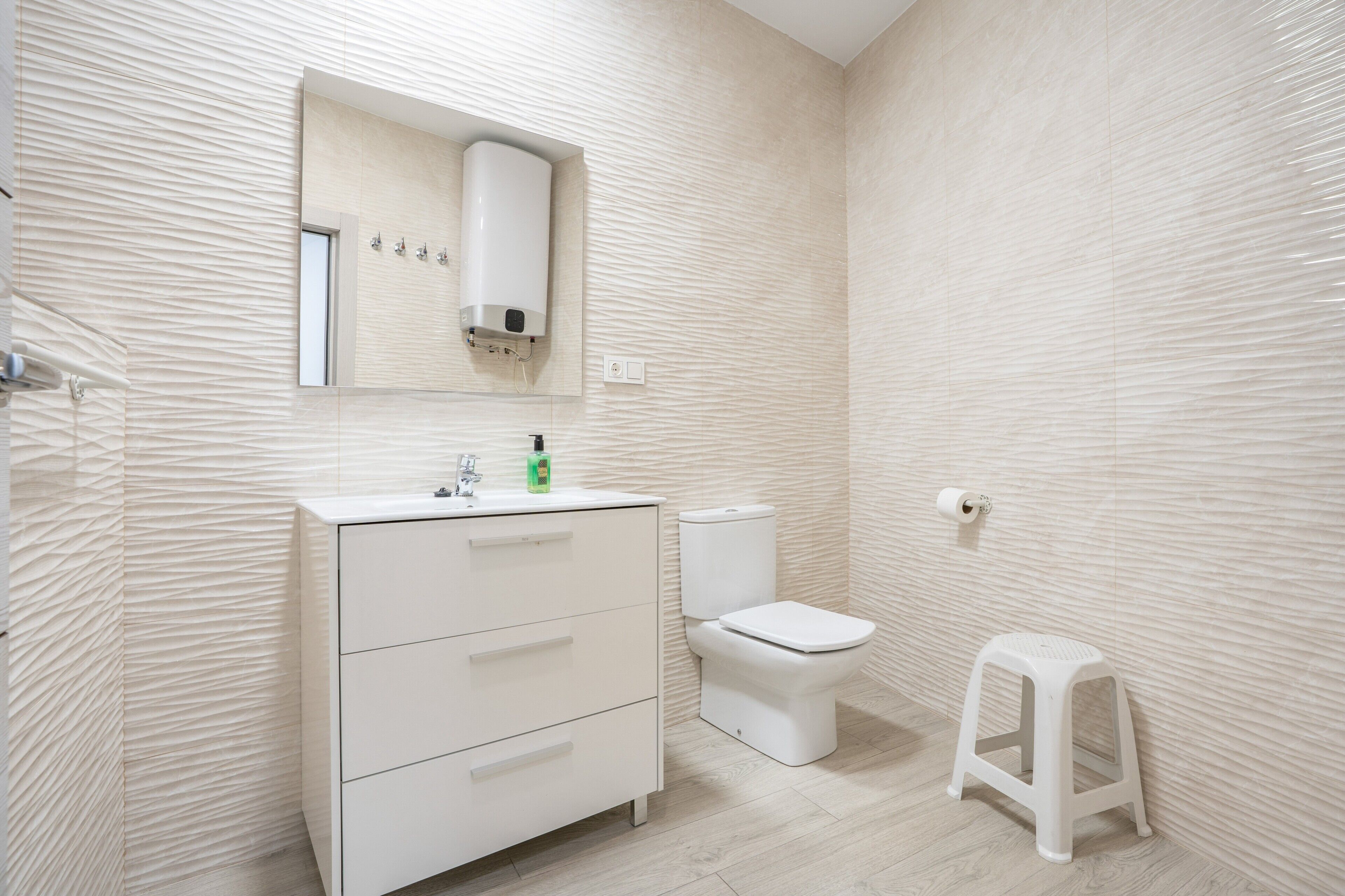 Un baño con tocador blanco, inodoro y un pequeño taburete.