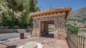 A stone structure with a tiled roof, a bench, and a decorative stone basin. - Apartment 'With Fireplace' with Mountain Views, Wi-Fi and Air Conditioning (Güejar Sierra)