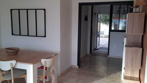 Zona pranzo con tavolo e sedie in legno, condizionatore d'aria a parete e un corridoio che conduce a una zona esterna.