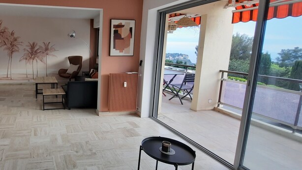 Un'ampia stanza con un'ampia porta scorrevole in vetro che si apre su una zona esterna con vista sul mare.