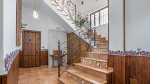 Una escalera con barandillas de metal decoradas, peldaños de madera y suelo de baldosas.