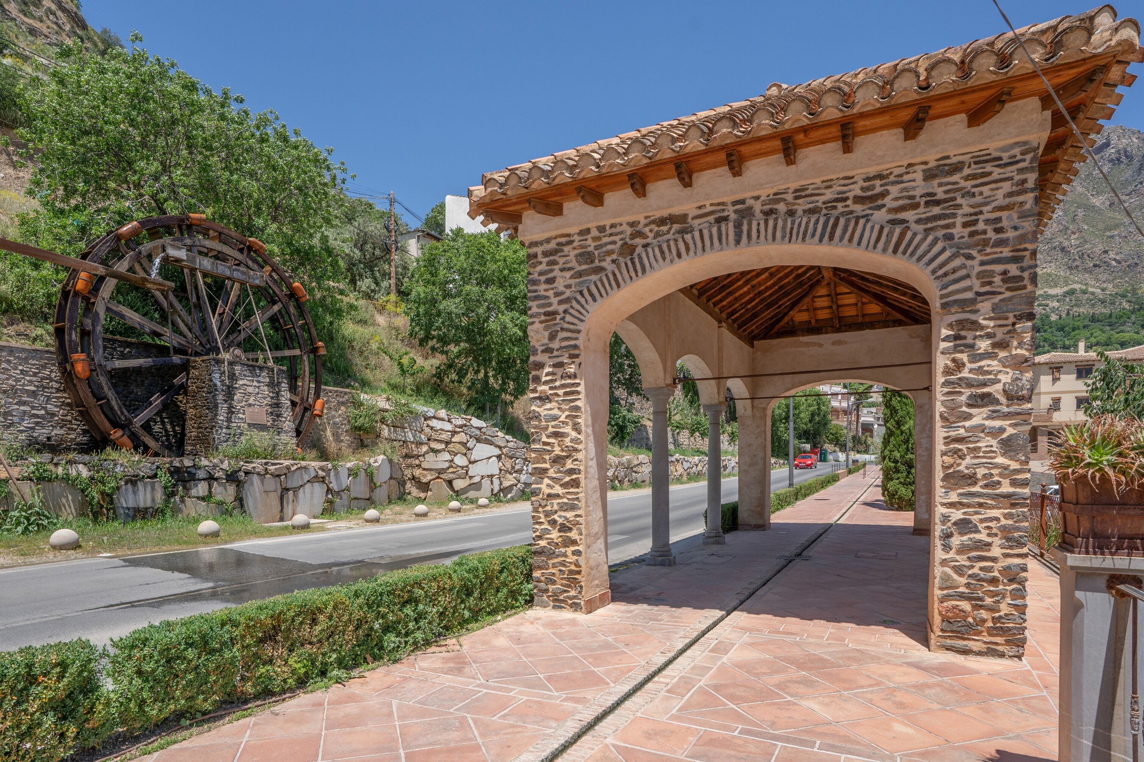 Una estructura de piedra con arcos, una rueda hidráulica y un camino empedrado.