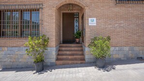 Un edificio de ladrillo con puerta de madera, escalones que conducen a la entrada y dos macetas a cada lado.