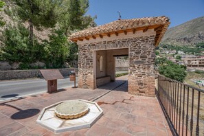 Una estructura de piedra con techo de tejas, un banco y una fuente decorativa de piedra.