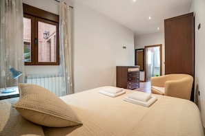 Un dormitorio con cama, una silla, cómoda y ventana con cortinas.