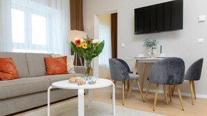 Una sala de estar moderna con un sofá, una mesa redonda con un jarrón de flores y un televisor de pantalla plana montado en la pared.
