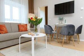 Ein modernes Wohnzimmer mit einer Couch, einem runden Tisch mit Blumenvase und einem an der Wand befestigten Flachbildfernseher.