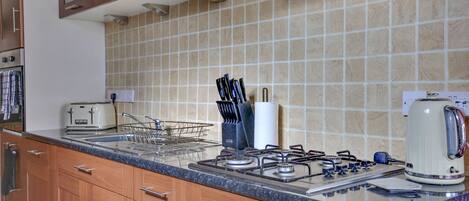 A kitchen with a gas stove, a kettle, a toaster, and a knife block.