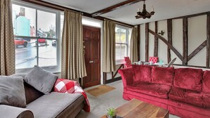 Een woonkamer met een grijze bank, een rode fluwelen bank, een houten salontafel en uitzicht op de straat door grote ramen.