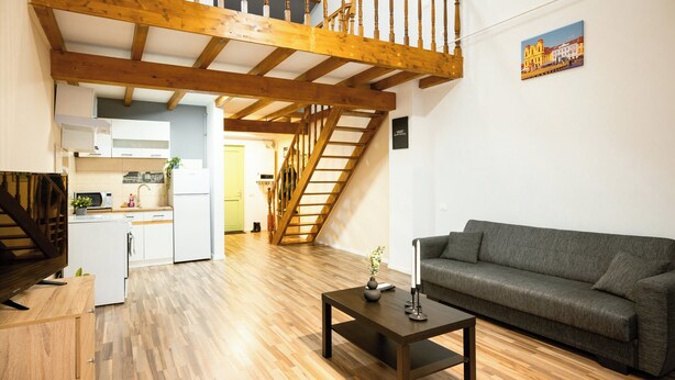 A spacious living area with a wooden staircase, a sofa, a coffee table, and a kitchen in the background. - Apartment Sleeps 4 With Pets Welcome (Timisoara)