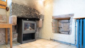 Ein rustikaler Raum mit Kamin aus Stein, Holzbalken und Fliesenboden.