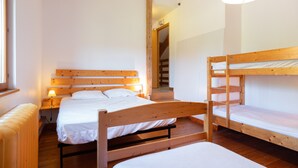 Ein Zimmer mit zwei Etagenbetten, einer Holzbank, einem Nachttisch mit Lampe und einer Treppe, die in ein weiteres Zimmer führt.