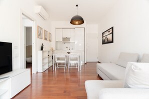 En moderne stue med en hvid sofa, et fjernsyn og et spiseområde med stole og et bord.