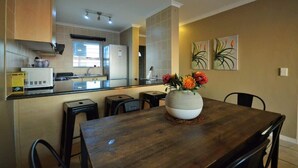A modern kitchen with a dining area, a refrigerator, a microwave, and a vase with flowers on the table. - Oceanfront Apartment w/Balcony, Table Mountain (Cape Town)