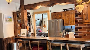 A rustic kitchen with wooden bar stools, a refrigerator, and a sign that reads 'Devil's Dip.' - Private 30-Acre Chalet - Hot tub,
Sauna, Trails (Townshend)