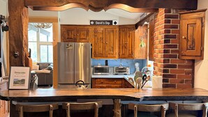 A kitchen with wooden bar stools, a refrigerator, a microwave, and a brick wall. - Private 30-Acre Chalet - Hot tub,
Sauna, Trails (Townshend)