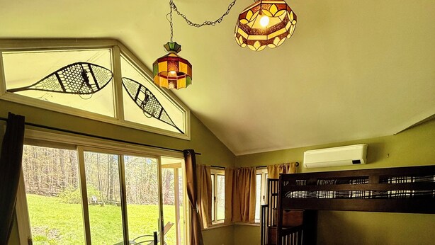 A room with a bunk bed, a large window with a view of a grassy area, and two hanging lamps. - Private 30-Acre Chalet - Hot tub,
Sauna, Trails (Townshend)