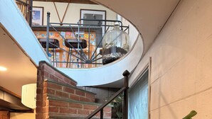 A spiral staircase with brick walls and metal railings, leading to a second floor with a dining area. - Private 30-Acre Chalet - Hot tub,
Sauna, Trails (Townshend)