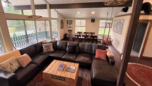 A cozy living room with a sectional sofa, a coffee table, and a dining area with a table and chairs. - Private 30-Acre Chalet - Hot tub,
Sauna, Trails (Townshend)