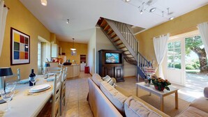 A spacious living area with a sofa, dining table, and a staircase leading to an upper floor. - PASTOUREAU (Sainte-Foy-de-Longas)