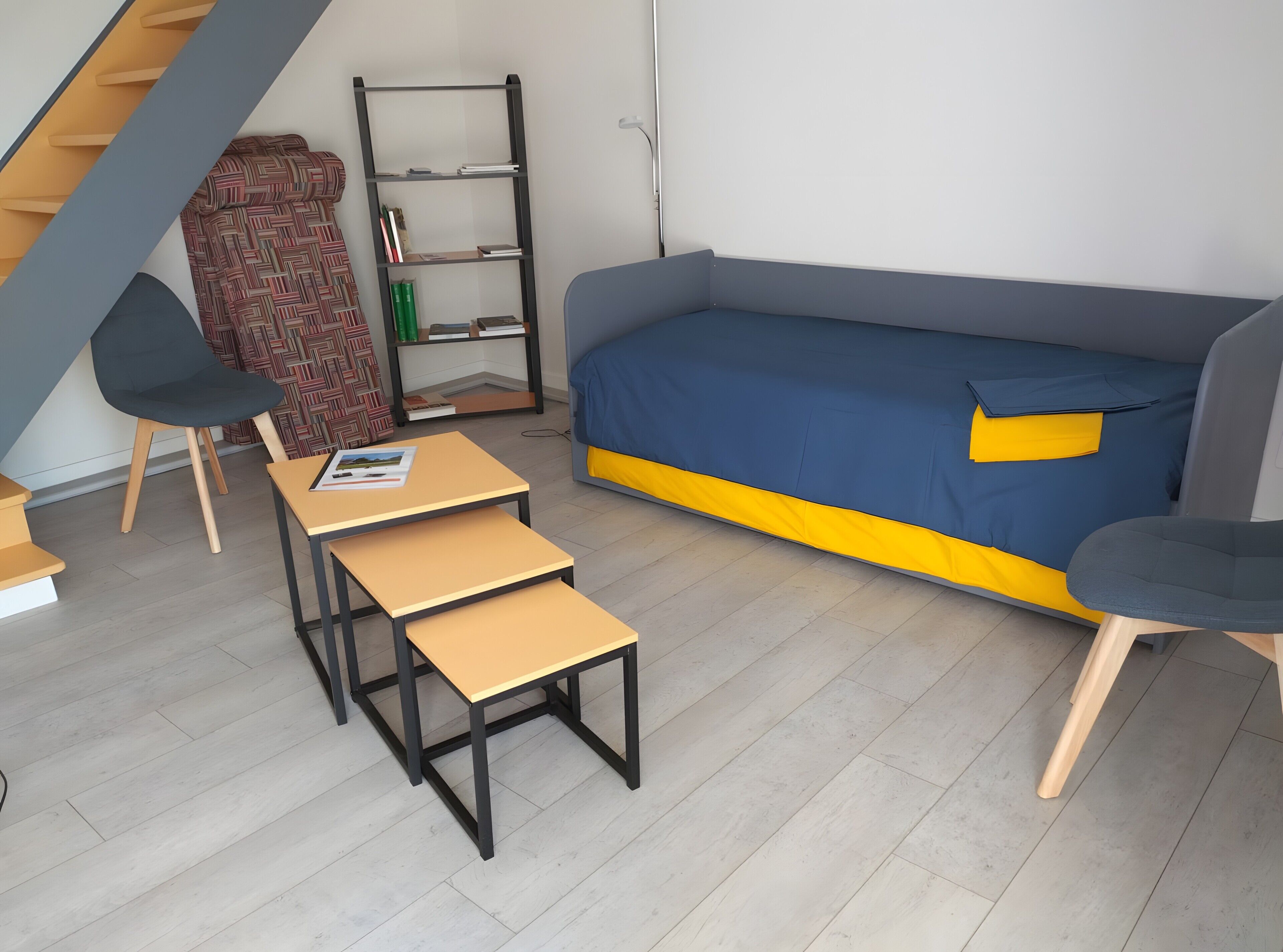A compact living space with a sofa, a small table, a chair, a bookshelf, and a patterned rug.