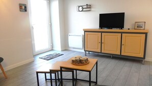 Una sala de estar con un televisor sobre un mueble bajo, una mesita con tazas, y una puerta que da a un balcón.
