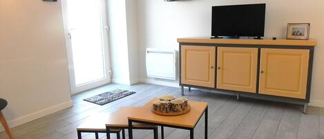A living room with a TV on a cabinet, a small table with cups, and a door leading to a balcony.