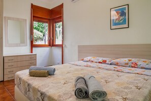 Ein Schlafzimmer mit Bett, Kommode, Fenster und einem gerahmten Bild an der Wand.