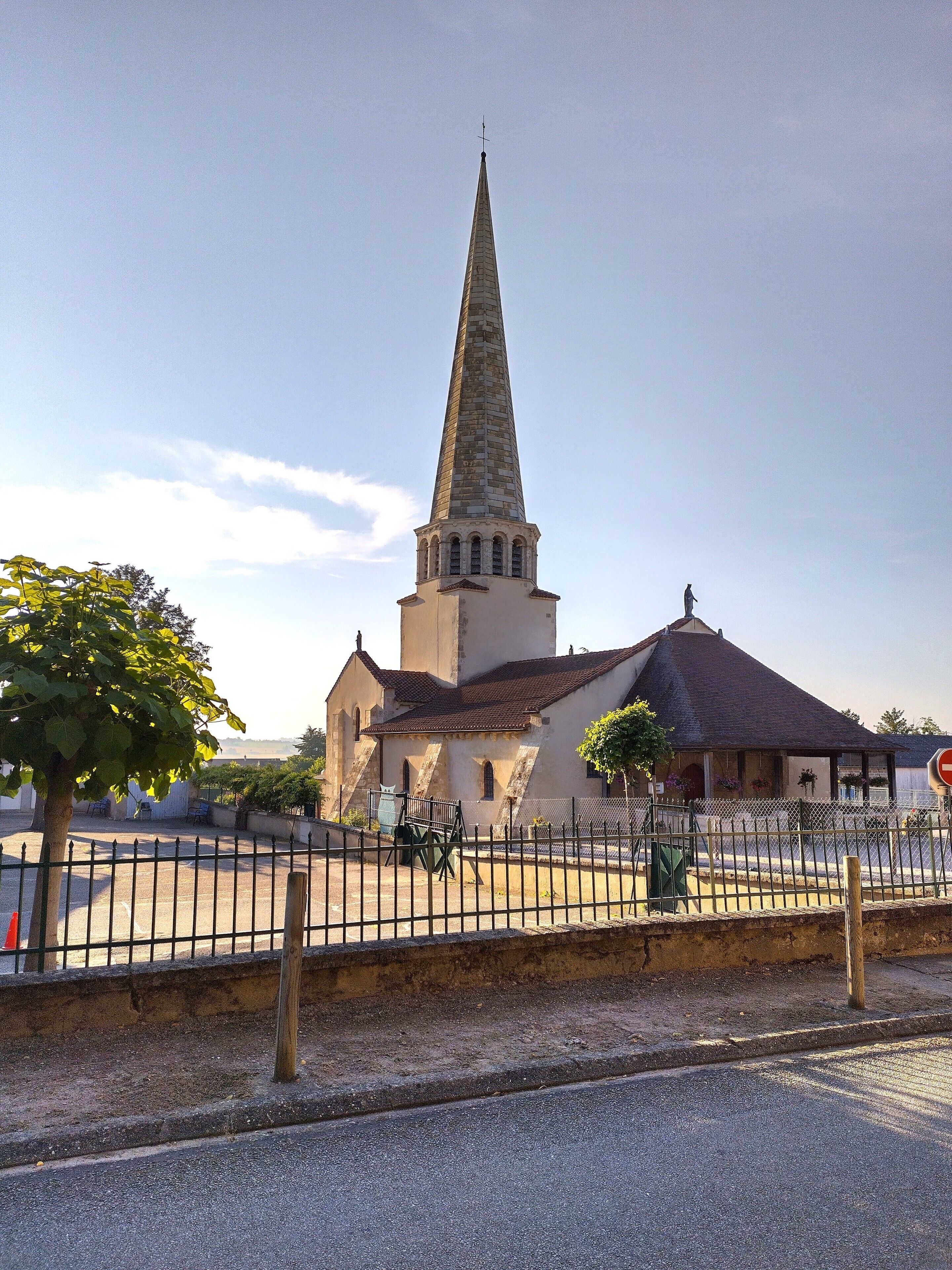 A church with a tall spire, a fenced courtyard, and a clear sky.