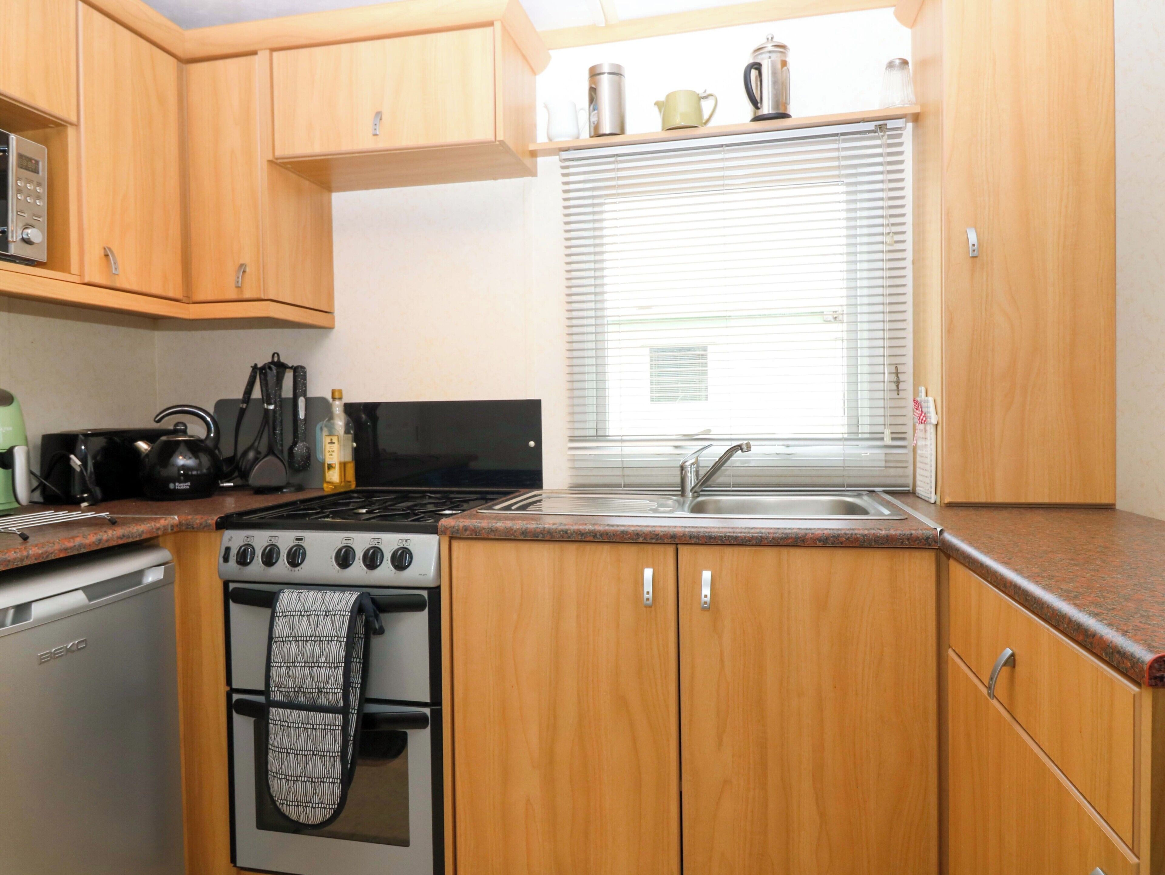 A kitchen with wooden cabinets, a stove, a sink, and a window with blinds.