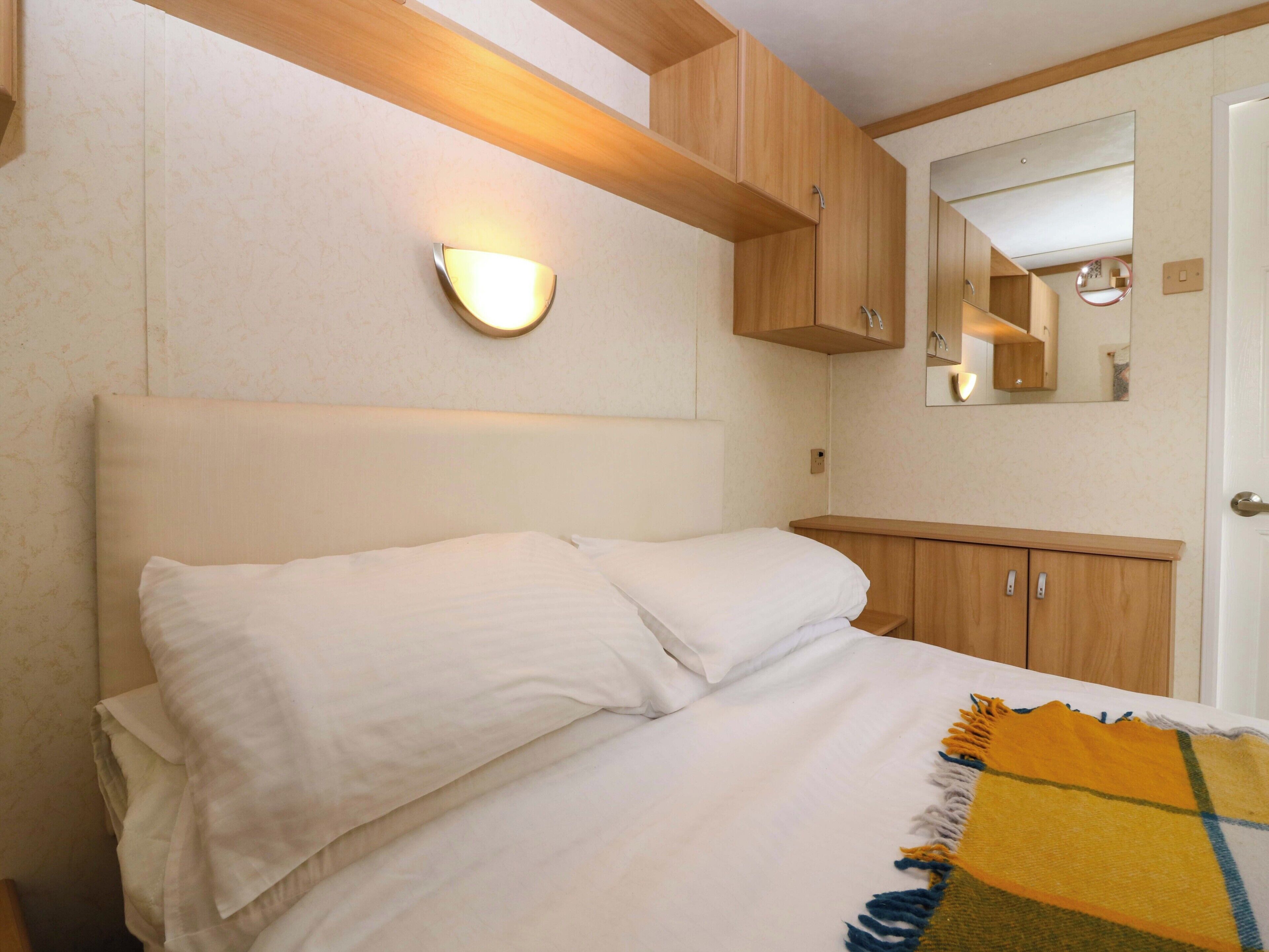 A bedroom with a bed, a nightstand, a mirror, and wooden cabinetry.