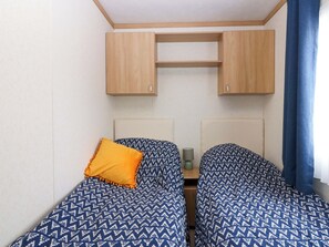 Un dormitorio con dos camas, cabecero de madera, una mesita pequeña y una estantería en la pared.