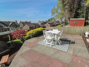 A patio with a table and chairs, surrounded by a wooden fence and a garden with red flowers.